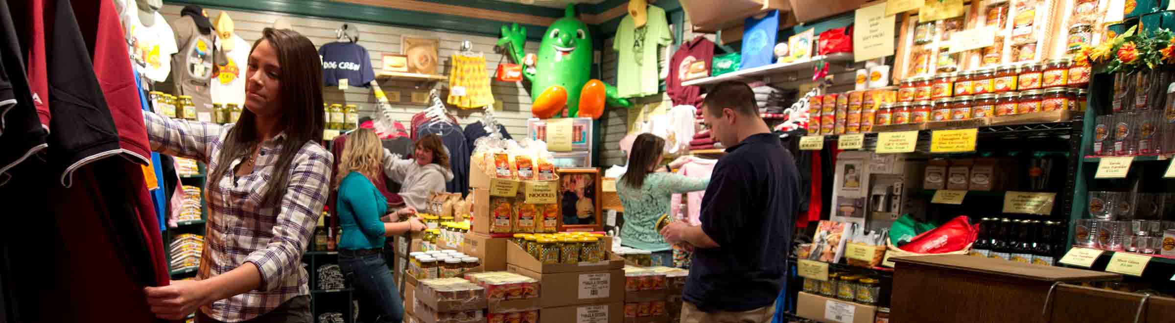 Five people browsing Tony Packo's physical gift shop; looking at tshirts, pickles, peppers and other Packo merchandise