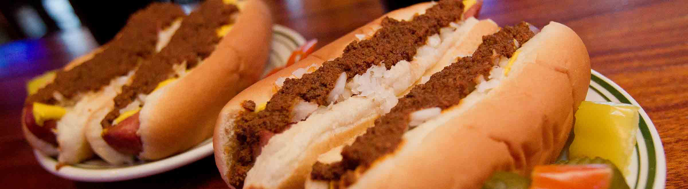 Close up of four Tony Packos Famous Hungarian Hot Dogs topped with Chili on plates